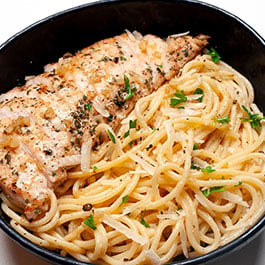 Sliced chicken breast on top of garlic butter pasta.