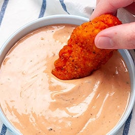 Dipping a chicken tender in an easy to make Cane's sauce recipe.
