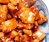 A close up image of teriyaki chicken bites in a decorated blue bowl.