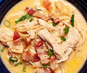 Chicken noodle soup with bacon in a blue bowl.