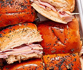 A tray of ham and cheese sliders on a blue and white napkin.