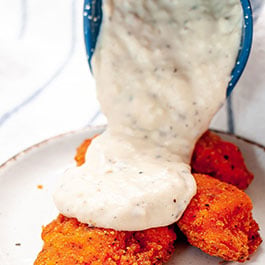 Pouring white gravy on fried chicken.