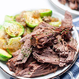 Roast beef on a small plate on top of a blue napkin.
