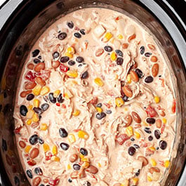 A pile of shredded chicken on top of the cream cheese chili in the slow cooker.